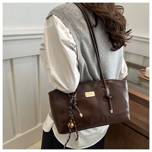 Detail of dark brown tote bag featuring golden hardware and decorative braided rope charm