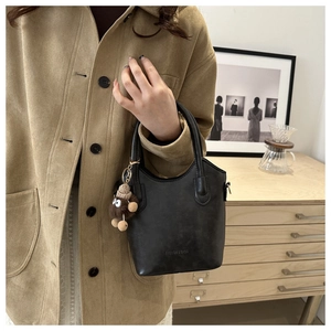 Detail of black matte leather tote bag with a cute brown plush monster pendant