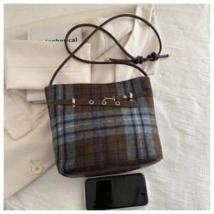 Detail of wool blend plaid bucket bag with brown leather strap and gold eyelet decor