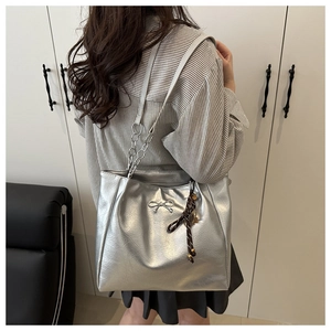 Detail of silver tote bag featuring a metallic bow, silk scarf, and chain strap