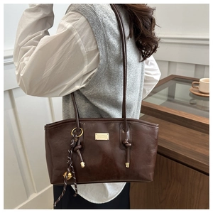 Detail of dark brown leather tote bag with gold metal plate and woven bell pendant charm