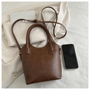 Flat lay of vintage brown bucket bag on beige blazer with 'FASHION & BAGS' lettering