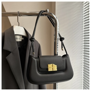 Detail of black matte leather baguette bag with a gold square buckle hanging on a rack