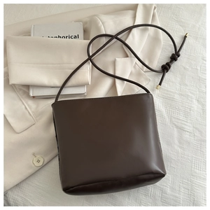 Detail of a brown leather bucket bag with decorative knotted strap and gold metal tips