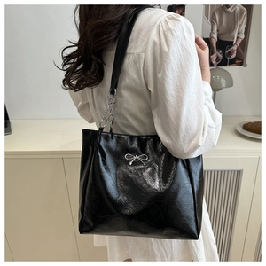 Close-up of black glossy tote bag with silver bow detail and chain strap