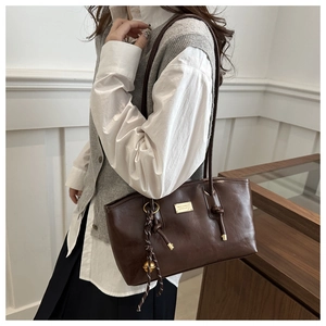 Detail of dark brown retro shoulder bag with golden bell charm and metallic logo plaque