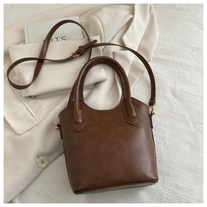 Detail of vintage dark brown bucket bag with adjustable strap on white blazer backdrop