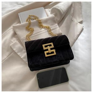 Detail of black suede shoulder bag with gold geometric lock and chain on blazer