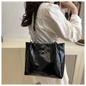 Detail of black glossy tote bag with silver bow accent and chain strap texture