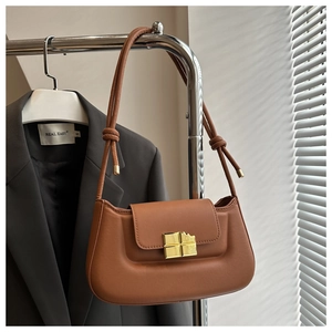 Detail of a brown leather shoulder bag featuring a unique gold square lock and knotted strap