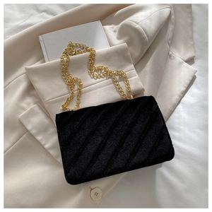 Close-up of black velvet crossbody bag with gold chain and diagonal quilted pattern