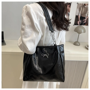 Detail of glossy black wrinkled leather tote bag with silver bow and chain strap