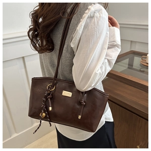 Detail of dark brown tote bag with gold metal plaque and polka dot bell charm