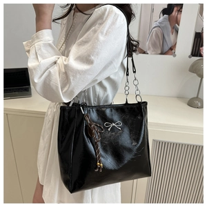 Close-up of shiny black tote bag with silver bow charm and chain shoulder strap detail