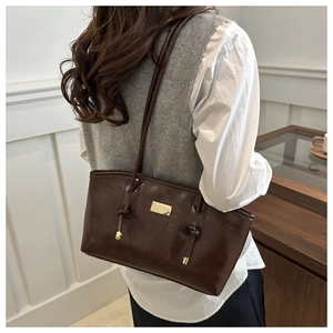 Detail of dark brown tote bag with glossy finish, gold logo plaque and knotted shoulder strap