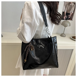 Detail of black tote bag with silver bow accent and woven tassel charm on a model