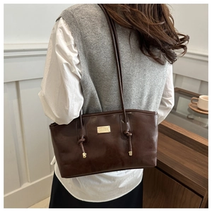 Detail of dark brown leather underarm bag with gold metal plate and knotted shoulder strap
