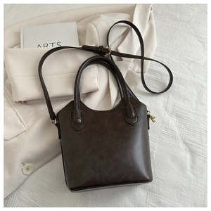Detail of dark brown vintage bucket bag with adjustable strap on cream blazer background