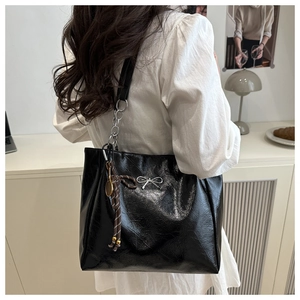 Detail of black tote bag with silver bow accent and woven charm on a model