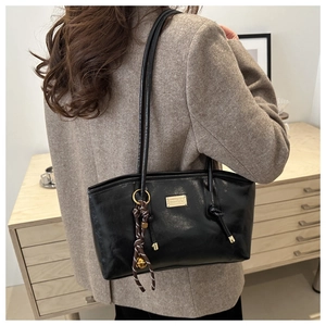 Detail of black faux leather tote with golden metal plate and woven rope knot accessory