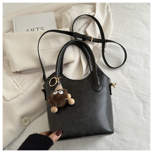 Detail shot of black leather bucket bag featuring plush charm and fashion text logo
