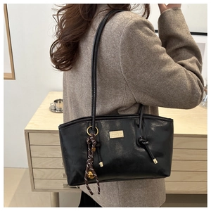 Close-up of black leather tote bag with gold logo plate and woven decorative charm