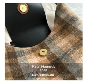 Detailed view of the magnetic snap closure on a plaid tweed tote bag with leather trim