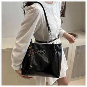 Close-up of black glossy tote bag with silver bow accent and striped silk ribbon detail