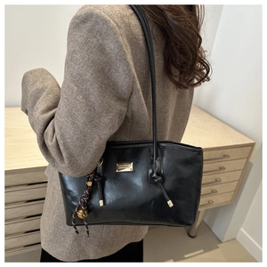 Detail view of black glossy leather underarm bag with gold logo plaque and woven charm