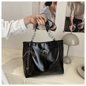 Detail of black tote bag with silver bow accent and chain strap in a cozy setting