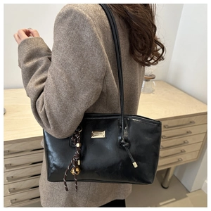Detail of black glossy tote bag with metal logo and woven charm on model's shoulder