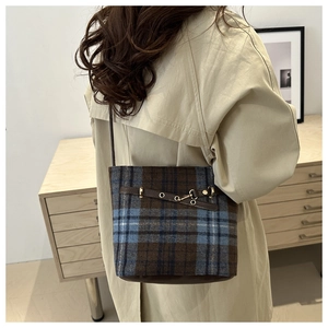 Detail of vintage plaid bucket bag with brown leather strap and gold buckle on a model