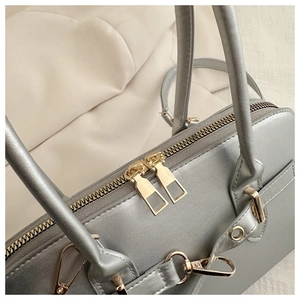 Detail of silver metallic handbag featuring premium golden double zippers and hardware