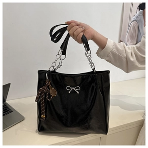Detail of black glossy tote bag featuring a silver bow buckle and tennis racket charm