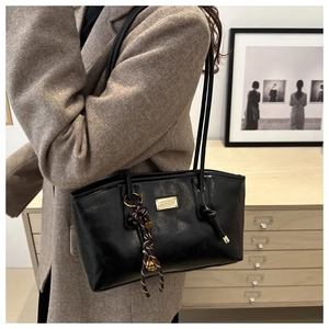 Detail of a black glossy tote bag with a golden metal nameplate and bell charm