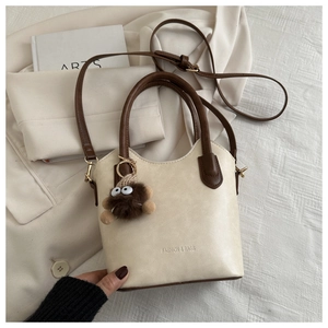 Detail view of cream PU leather bucket bag with brown handles and plush monster charm