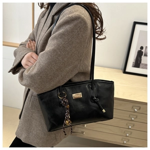 Detail of black wax leather tote with gold metal plaque and woven charm on wool coat