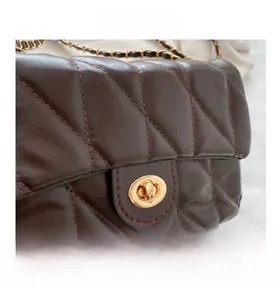 Macro shot of dark brown quilted leather bag with golden oval twist lock and metal chain