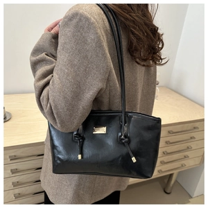 Detail of black glossy leather tote bag with gold metal plate and knotted leather design