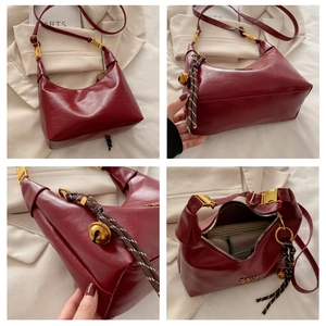 Detail view of burgundy crescent hobo bag with gold hardware and woven bell charm
