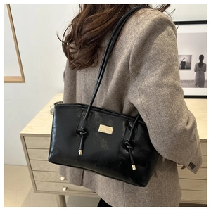 Detail of black glossy leather underarm bag featuring gold logo and knot shoulder strap