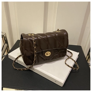 Détail du sac à chaîne matelassé marron foncé avec fermoir tournant doré sur un livre