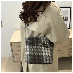 Detail of wool bucket bag featuring green and brown plaid pattern with leather strap