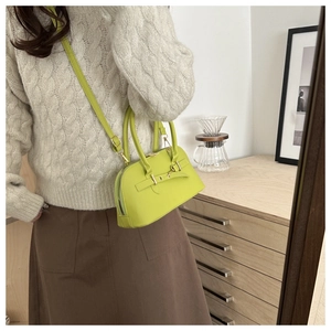 Close-up of a neon green bowling-style crossbody bag with gold hardware in a cozy interior