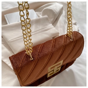Close-up of brown velvet shoulder bag with quilted pattern and gold chain strap
