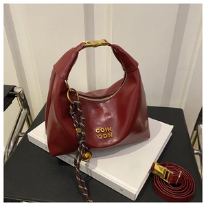 Deep red saddle bag with gold hardware, bell charm, and a detachable shoulder strap