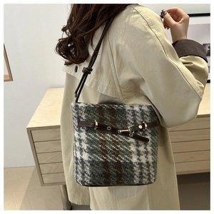 Detail view of plaid tweed bucket bag in dark green and coffee on model's shoulder