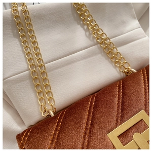Detail of brown velvet crossbody bag featuring quilted texture and gold chain strap