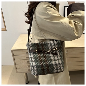 Detail of tweed bucket bag with leather trim and gold buckle on a beige trench coat