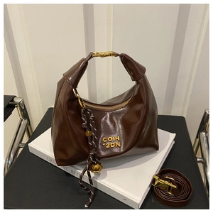 Detail view of deep brown gloss crescent hobo bag with gold hardware and woven charm